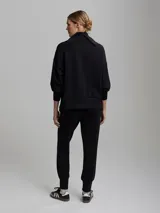 Buzo negro de corte oversize con cuello alto, mangas abullonadas, cierre lateral y hombros caídos.