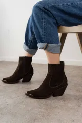 Bota corta de cuero gamuzado color marrón oscuro, con punta fina y detalle metálico. Tiene cierre lateral y taco de madera.
