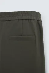 Pantalón verde oscuro de corte recto, con cintura elástica, bolsillos laterales y un bolsillo trasero. Cierre frontal con cremallera y botón.