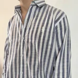 Camisa celeste y blanca a rayas verticales, de manga larga con puños abotonados y cuello clásico.