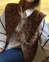 Chaleco marrón con estampado geométrico en tonos rojo y azul. Tiene cuello alto y cierre frontal con botones dorados.