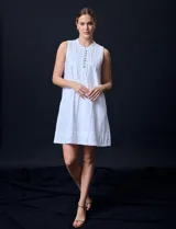 Vestido corto blanco de algodón y rayón, sin mangas, con cuello a la base, abertura central con botones y detalle plisado en la delantera. Incluye bolsillos laterales.