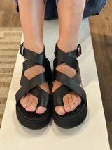Sandalias negras de cuero con tiras cruzadas y hebilla lateral.