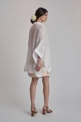 Camisa blanca de lino con cuello clásico, cierre frontal con botones y mangas anchas 3/4. Presenta detalles de bordado calado en el frente y puños.