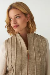 Chaleco color crema con cuello alto y cierre frontal con cremallera. Diseño con alforzas verticales en la parte superior delantera y trasera.