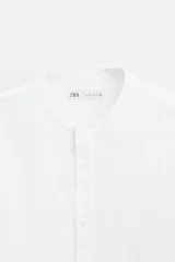 Camisa color beige claro, de corte relaxed fit, confeccionada en tejido de lino y algodón. Tiene cuello mao, manga larga con puños abotonados y cierre frontal con botones.