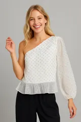 Blusa blanca asimétrica con un hombro descubierto, manga larga abullonada y estampado de lunares plateados.