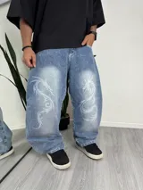 Pantalón de jean azul claro, corte holgado, con estampado de dragones blancos en ambas piernas.