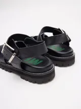 Sandalias romanas color verde oliva, con tiras entrecruzadas y hebilla lateral. Suela de goma negra con plataforma de 3cm. Fabricadas en cuero vacuno.