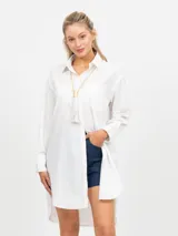 Vestido camisero largo, color blanco, de manga larga y cuello solapa. Presenta un bolsillo delantero de plastrón y bajo asimétrico.