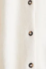 Cárdigan de punto color crema, de manga larga, con cuello redondo y cierre frontal de botones oscuros.