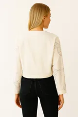 Chaqueta color crema con estampado de flores en color gris, de corte cropped, con cuello camisero, cierre frontal con botones a tono, mangas largas y bolsillos tipo parche en el pecho.