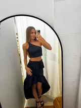 Pollera de tafeta color azul marino con diseño asimétrico de tipo high-low y volados. Presenta una cintura entallada y gran volumen en el ruedo.