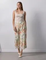 Pantalón capri de lino color crudo con estampado de hojas en tonos verdes, amarillos y naranjas. Presenta bolsillos laterales y detalle de puntilla en el ruedo.