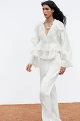 Camisa blanca de cuello redondo con escote en V y mangas largas acampanadas con volantes.