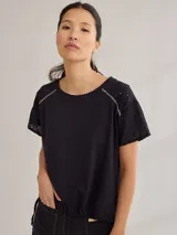 Remera negra de algodón con mangas cortas con detalle de calado y bordado en los hombros y mangas. Corte recto con cintura ajustable con cordón.