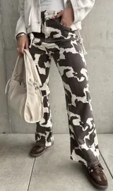 Pantalón de jean de corte recto con estampado de manchas de vaca en tonos marrón y blanco.