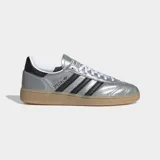 Championes Adidas Handball Spezial de caña baja, con exterior de cuero sintético metalizado color plata y tres franjas laterales negras. Presentan detalles en negro en el talón y cuello, cordones blancos y suela de caucho color caramelo.