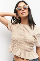 Remera negra de algodón con cuello redondo y mangas cortas. Presenta fruncidos en la cintura.