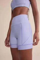 Short deportivo de tiro alto color lila, con tecnología de compresión, protección solar UV 50+, forro estratégico para evitar transparencias, dos bolsillos laterales sin costuras visibles y barra con gripper para un ajuste seguro.