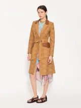 Trench marrón claro con broderie y detalles en cuero marrón, con hombreras, bolsillos plaqué con tapa de cuero y lazo para ajustar en cintura.