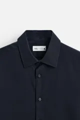 Camisa blanca de corte regular, cuello italiano, manga larga con puños abotonados y cierre frontal con botones.