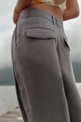 Pantalón negro de tiro alto con trabillas, doble pliegue, bolsillos laterales y tapetas en la espalda. Tiene pernera ancha y cierre frontal con cremallera y gancho metálico.