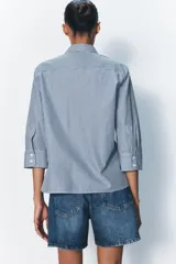 Camisa de cuello solapa y manga tres cuartos con puño ancho. Tiene aberturas laterales en el bajo y cierre frontal con botones ocultos.