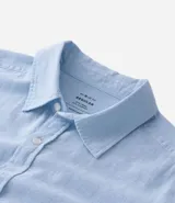 Camisa celeste de lino con cuello camisero, abotonadura frontal y mangas largas.