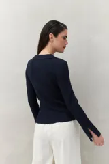Sweater blanco de punto acanalado con cuello tipo polo y botonadura frontal de botones metálicos. Mangas largas con terminación en pequeñas aberturas.