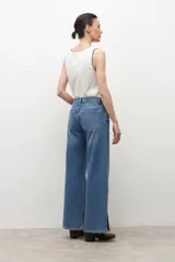 Pantalón de jean de tiro alto, color azul medio, con corte ancho y recto, y aberturas laterales en el ruedo.