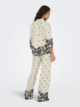 Camisa color crema con estampado de hojas y flores negras, cuello camisero, mangas 3/4 amplias y cierre frontal con botones.