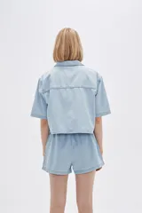 Camisa celeste de jean, corte cropped, con cuello camisero, cierre frontal con botones y mangas cortas.
