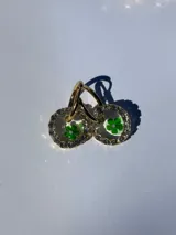 Aros dorados con dije circular de resina y strass, con flor de vidrio verde en el interior. El arito es de acero quirúrgico.