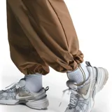 Pantalón cargo color crema, de corte ancho y tiro alto, con cintura elástica ajustable y bolsillos laterales con solapa. Logo de Nike bordado en blanco en el muslo izquierdo.