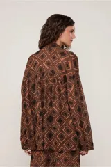 Camisa marrón con estampado geométrico de rombos negros, cuello alto, manga larga, cierre de botones, canesú con sisa descentrada y corte fruncido.