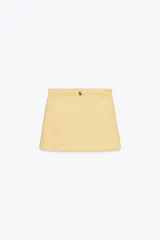 Minifalda color amarillo pálido de tiro alto con cinturón del mismo tejido y hebillas metálicas. Cierre trasero con cremallera oculta.