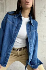Sobrecamisa de denim azul con bordados florales en cuello y hombros, cierre frontal con botones azules y corte holgado.