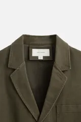 Blazer color verde oliva de algodón con efecto lavado, corte relaxed fit, cuello con solapas de muesca, manga larga y bolsillos frontales de plastrón. Cierre frontal con dos botones.