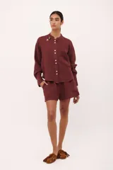 Camisa de lino color vino tinto, con cuello mao y botones blancos. Presenta un corte holgado y manga larga con puños abotonados.