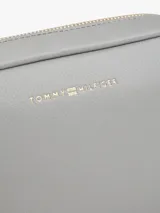 Cartera bandolera rectangular de cuero sintético color gris claro, con cierre superior de cremallera y logo metálico de Tommy Hilfiger en el frente.