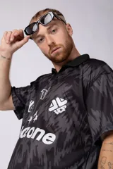 Camiseta de fútbol negra con estampado abstracto en gris, cuello tipo chomba y logos estampados en el frente.