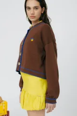 Cárdigan tejido en 50% algodón y 50% acrílico, color crema, con pespuntes tejidos en contraste color borgoña y bordado de limón en el pecho. Tiene cuello con volados, cierre frontal con botones y corte relajado.