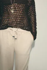 Pantalón color beige de tiro medio con cintura elástica ajustable con cordones, bolsillos delanteros y falsos bolsillos de vivo en la espalda. El bajo es ajustable con botón a presión.