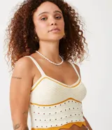 Top cropped de punto color crema con detalles de rayas contrastantes en color mostaza. Presenta escote en V, tirantes finos regulables y un diseño texturizado con calados. El bajo es festoneado y ondulado.