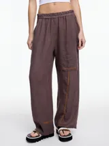 Pantalón de lino color marrón con calce relajado y elástico en la cintura. Incluye bolsillos laterales y un bolsillo invertido. Presenta detalles de bordado tipo pespunte en color contraste en la pierna y el bajo.
