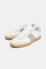 Zapatillas deportivas blancas con detalles en celeste y suela color caramelo.