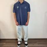 Chomba azul de piqué con cuello clásico y manga corta. Presenta bordados blancos con motivos de golf en el pecho.