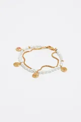 Pulsera dorada de doble cadena, una de eslabones y otra de perlas, con dijes colgantes tipo moneda y cierre de mosquetón.