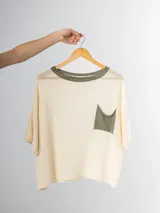 Remera tejida en hilo italiano, color beige, con cuello a la base y bolsillo frontal. De caída relajada y silueta amplia.